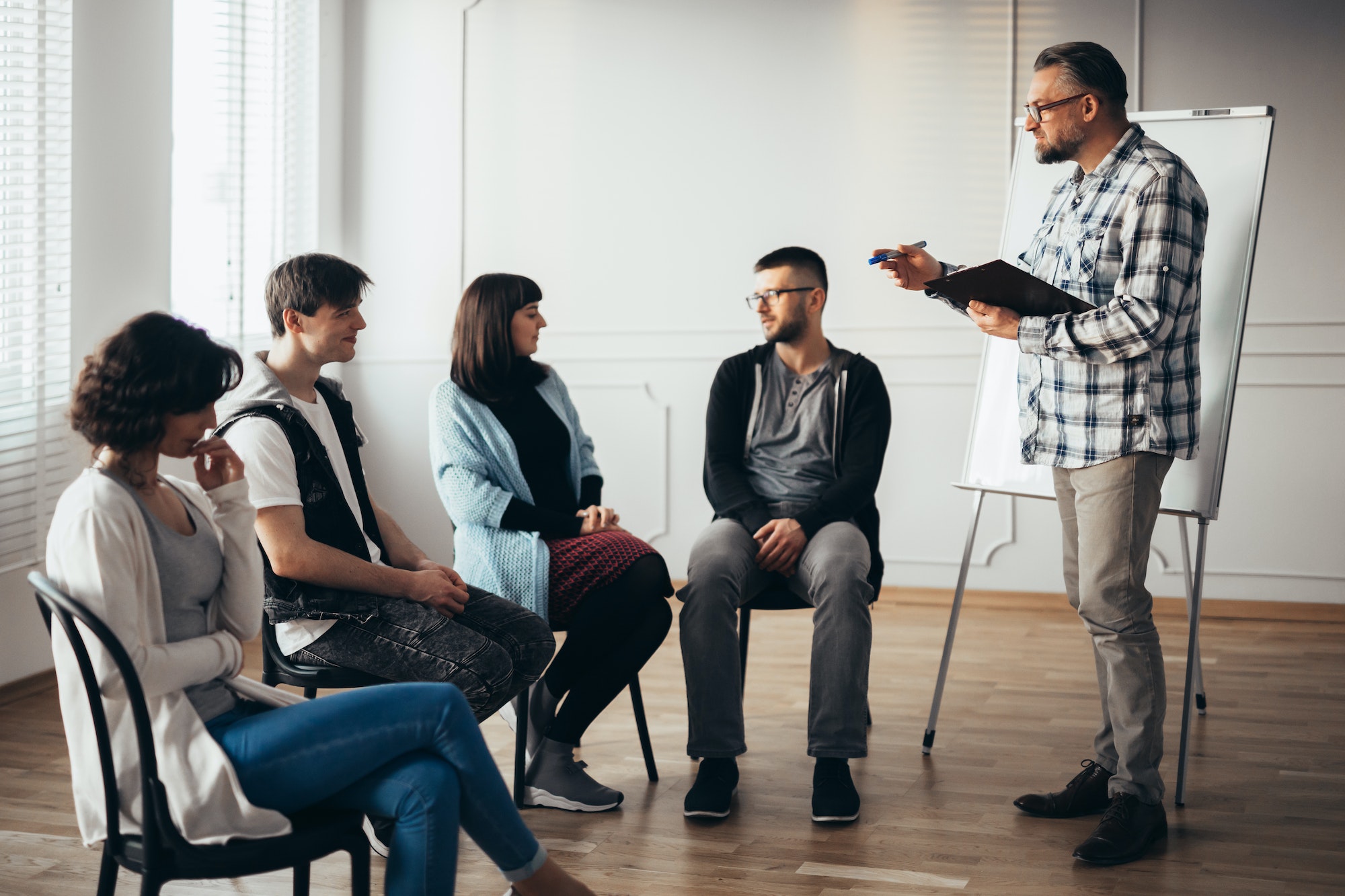 therapist stands in front of a group of people of different ages during meeting for people